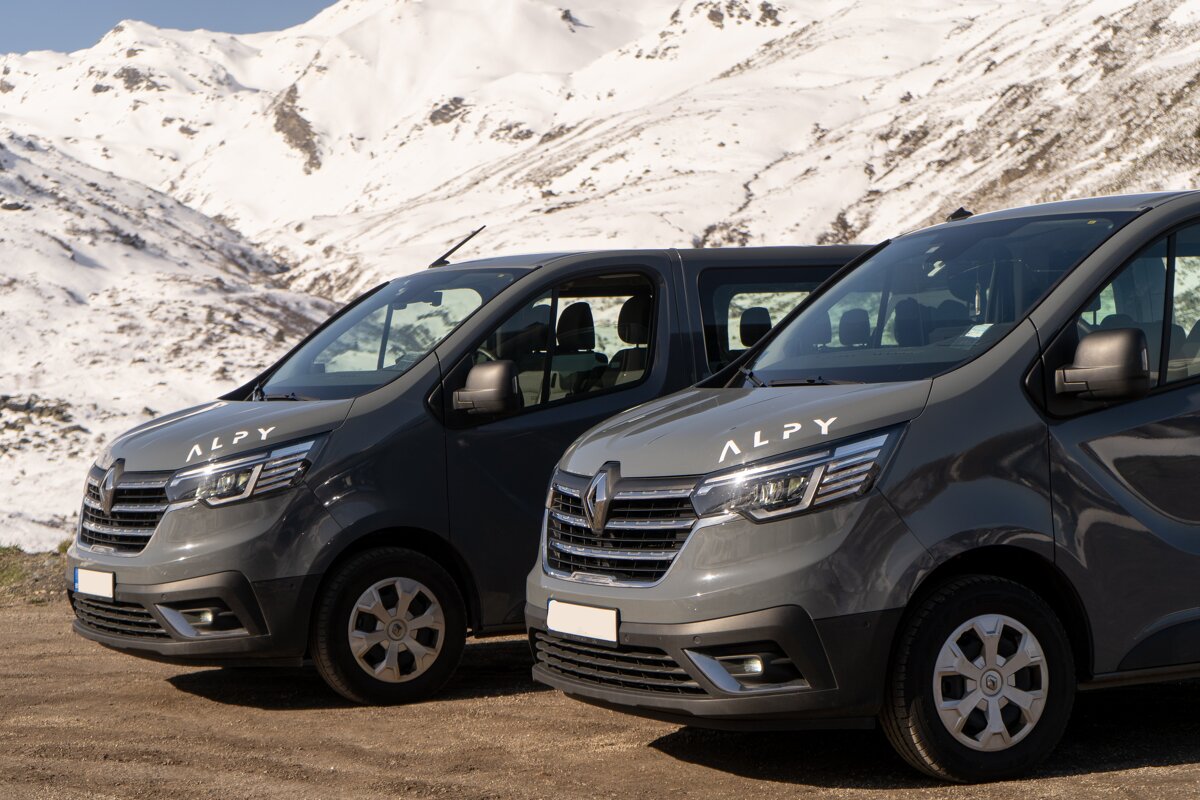 Two alpy vans are parked in front of a snowy mountain