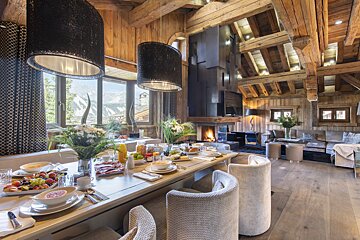 A lavish, rustic wooden chalet interior featuring a long breakfast table, a cozy living area with a fireplace, and stunning mountain views.