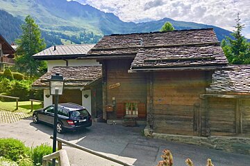 A car is parked in front of a wooden house with a mountain in the background