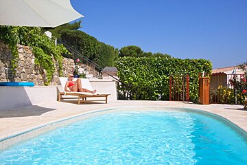 A woman sits on a lounge chair near a swimming pool