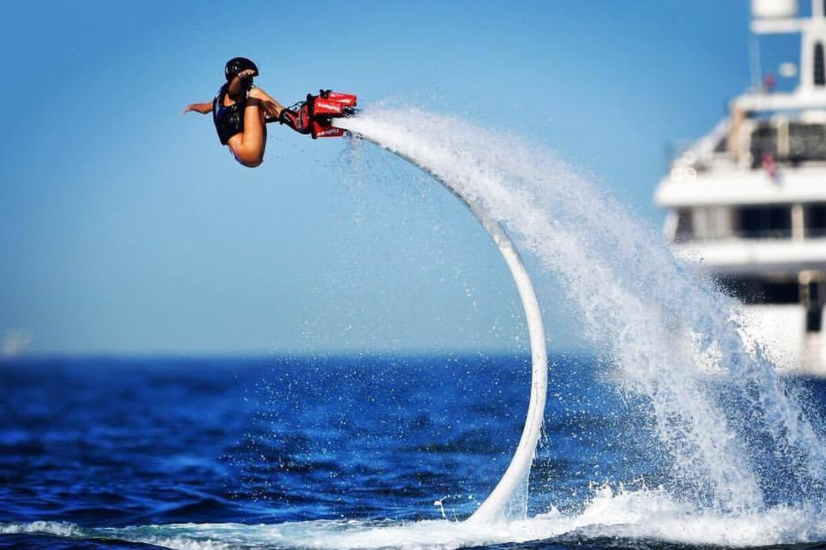 a girl flyboarding with yacht in background