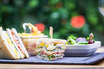 A sandwich with a toothpick in it sits on a tray next to a basket of french fries