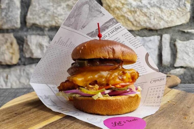 A sandwich is wrapped in newspaper and has a toothpick sticking out of it that says let 's rock