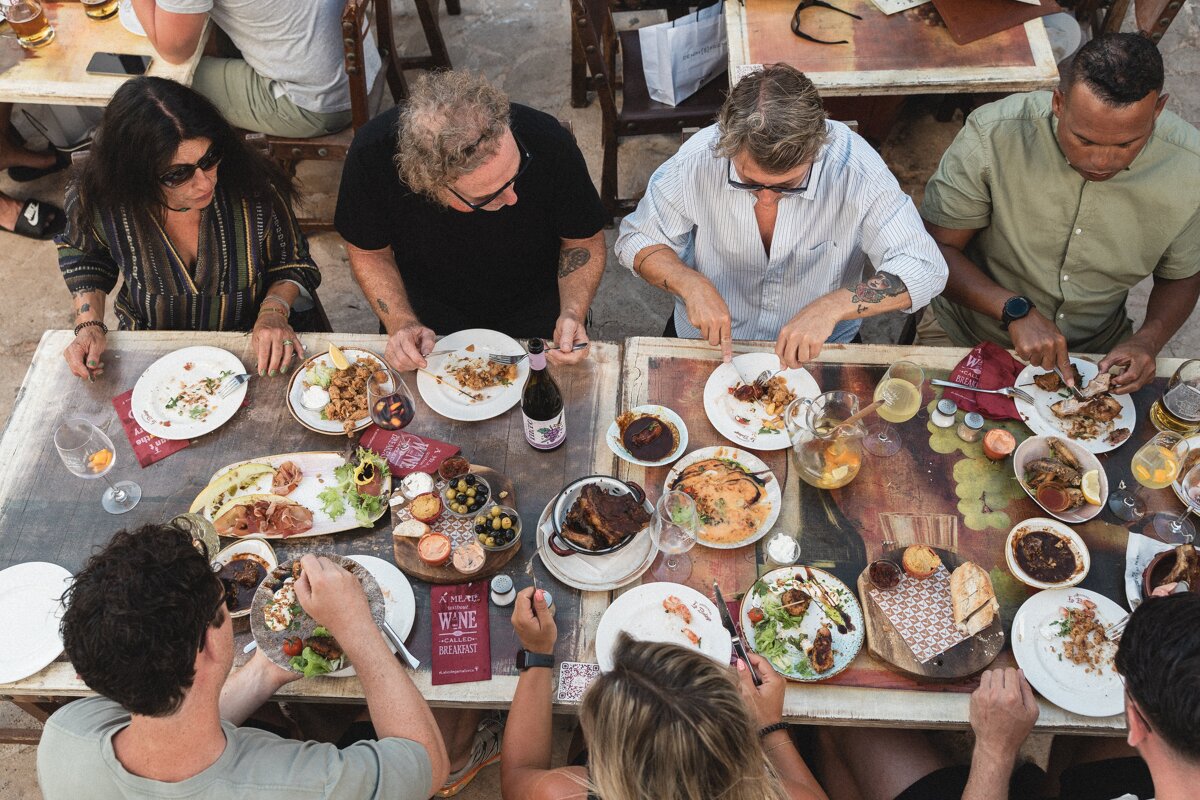 A group of people sitting at a table with plates of food and a menu that says being
