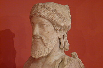 A statue of a man with a beard is against a red wall