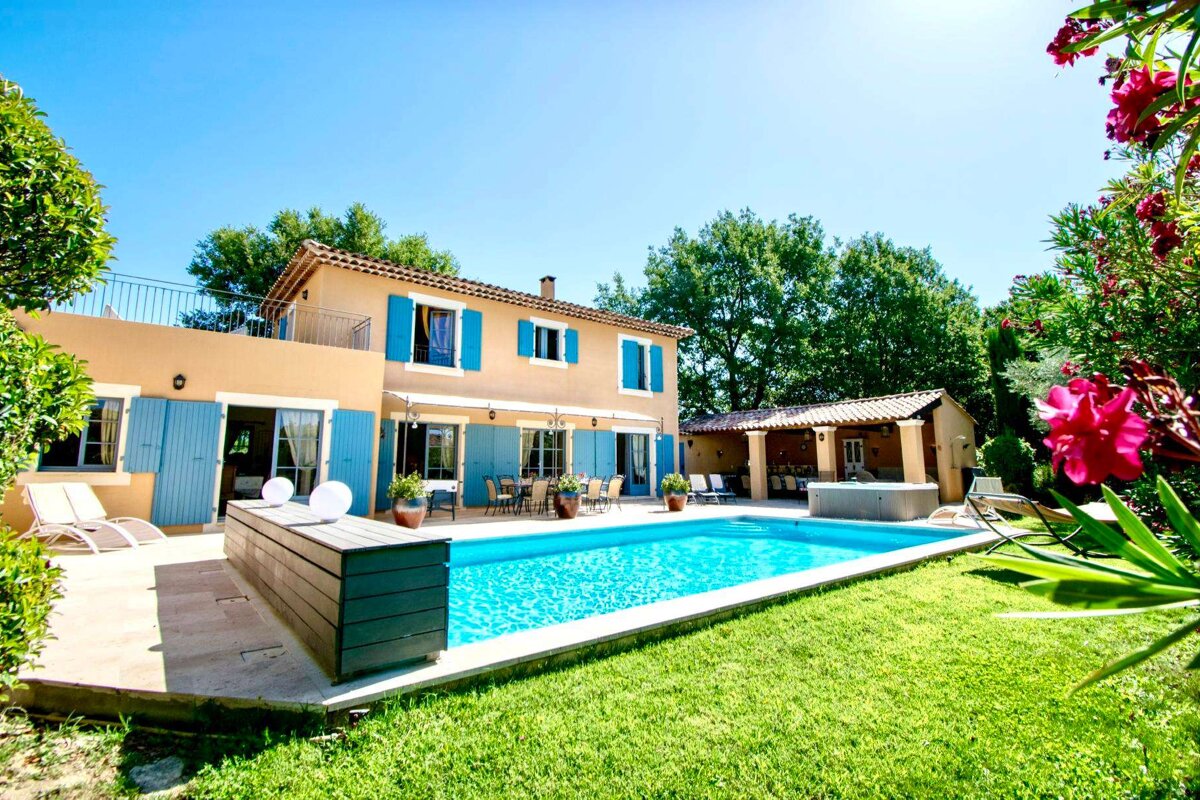 A house with blue shutters has a large swimming pool in front of it