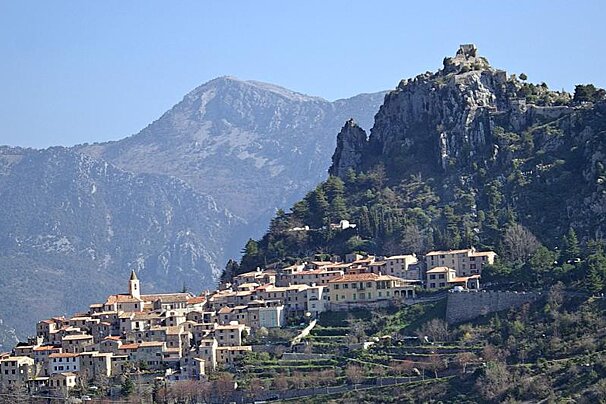A small town sits on top of a hill with mountains in the background