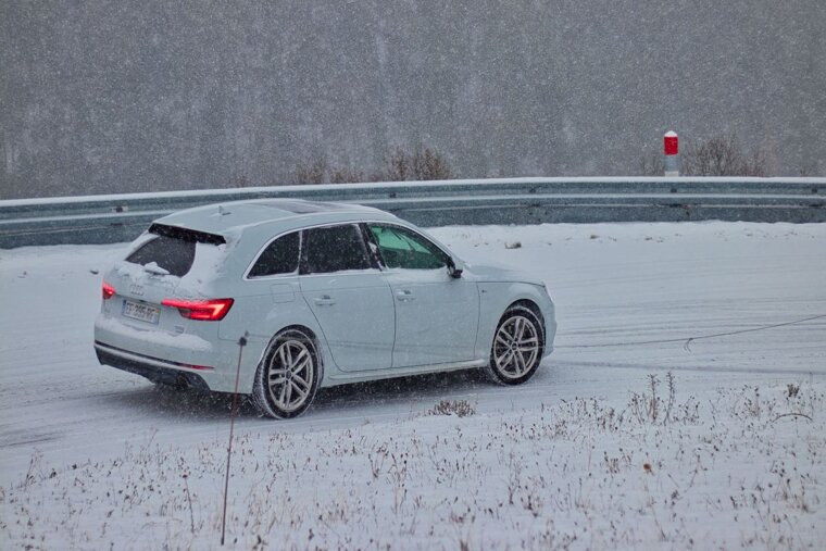 A white audi is driving on a snowy road