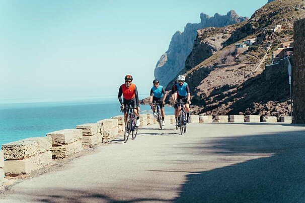 A group of cyclists are riding down a road near the ocean