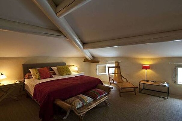 A bedroom with a bed , chair , table and lamp