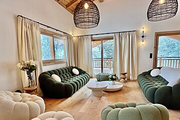 A stylish living room with unique green bubble sofas, light wood floors, and large windows overlooking a snowy forest. Woven light fixtures add warmth.