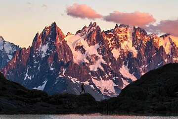 A person standing on a rock in front of a snowy mountain