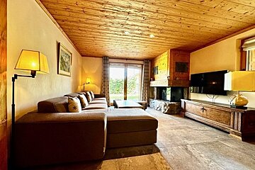 A cozy living room with a large sofa, wooden ceiling, fireplace, TV, and warm lighting.