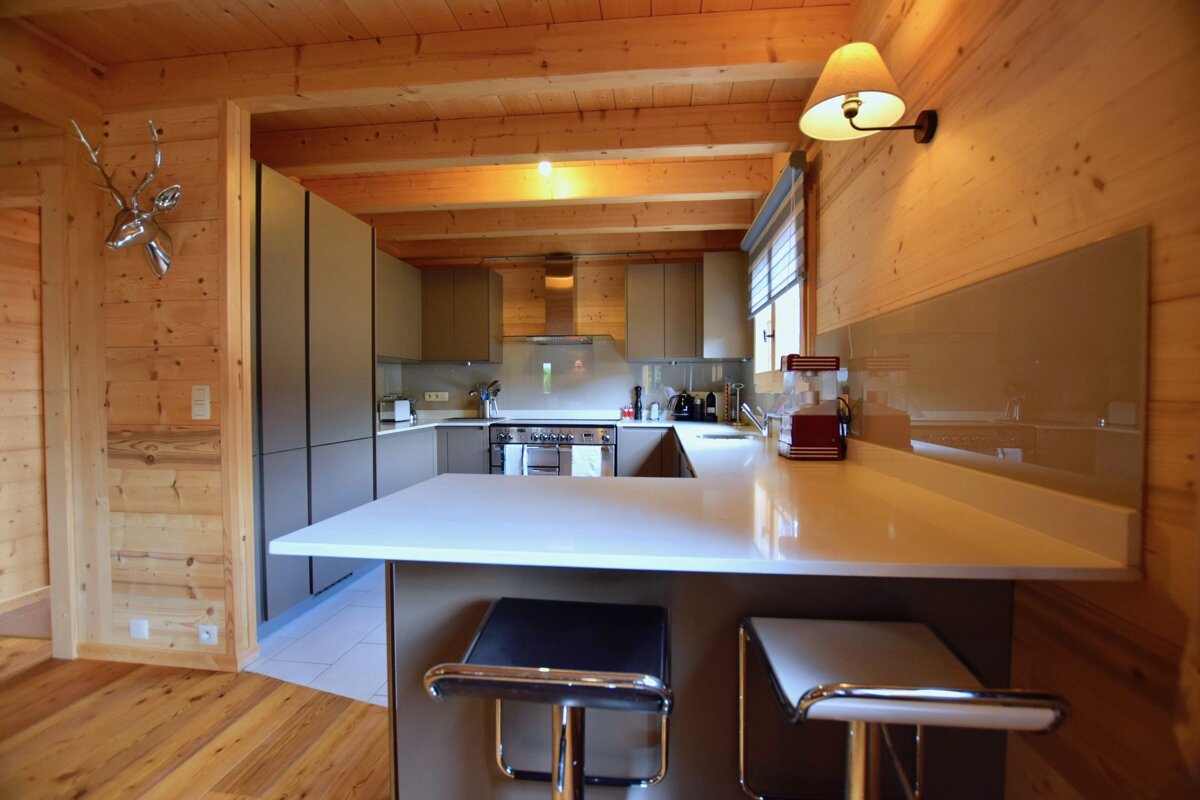 A stylish, modern kitchen with light grey cabinets and a bar, set within a rustic wooden cabin, complete with a silver deer head.