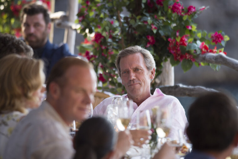 A man in a pink shirt sits at a table with wine glasses