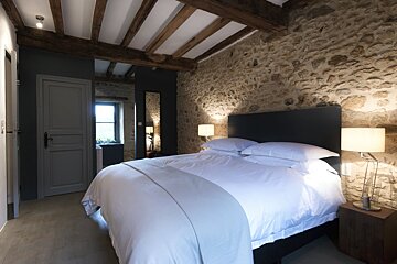 A bedroom with a stone wall and a bed with white sheets