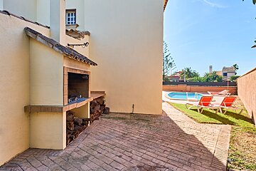 A brick patio with a bbq and a pool in the background