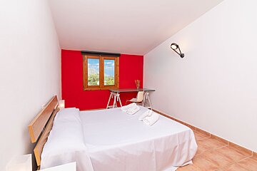 A bedroom with a red wall and a white bed