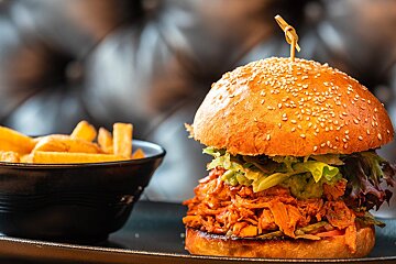 A hamburger with a toothpick in it sits next to a bowl of french fries