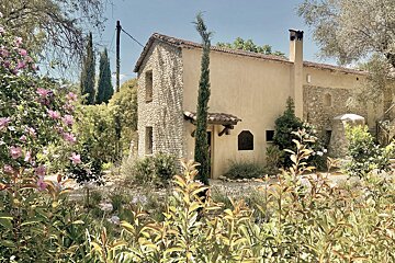 A stone house is surrounded by flowers and trees
