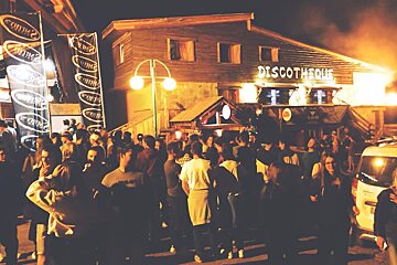 A lively crowd gathers outside a wooden 