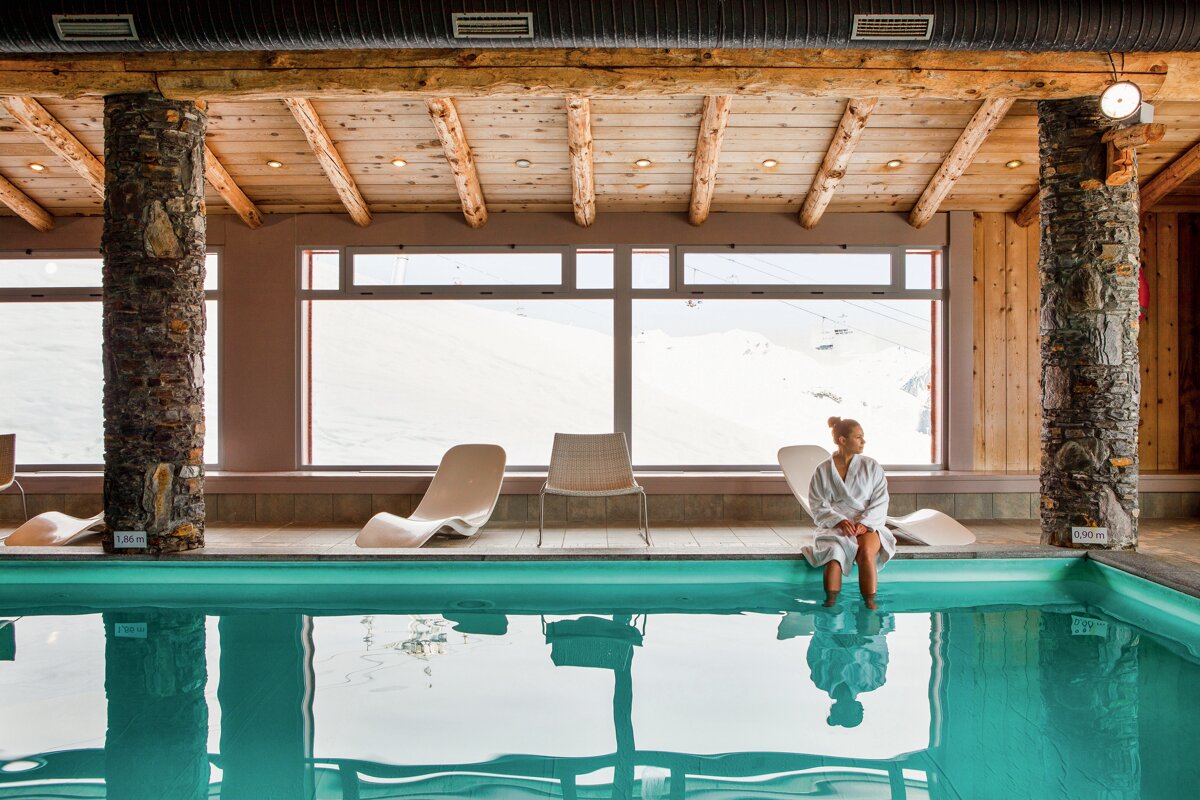 A woman in a bathrobe sits on the edge of a swimming pool