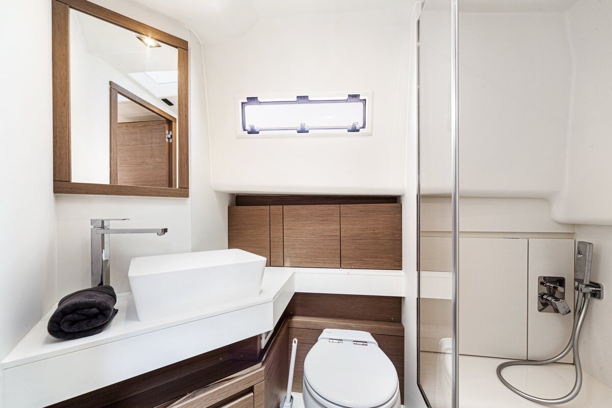 Compact, modern yacht bathroom featuring a white vessel sink, wood-framed mirror, toilet, and glass-enclosed shower.
