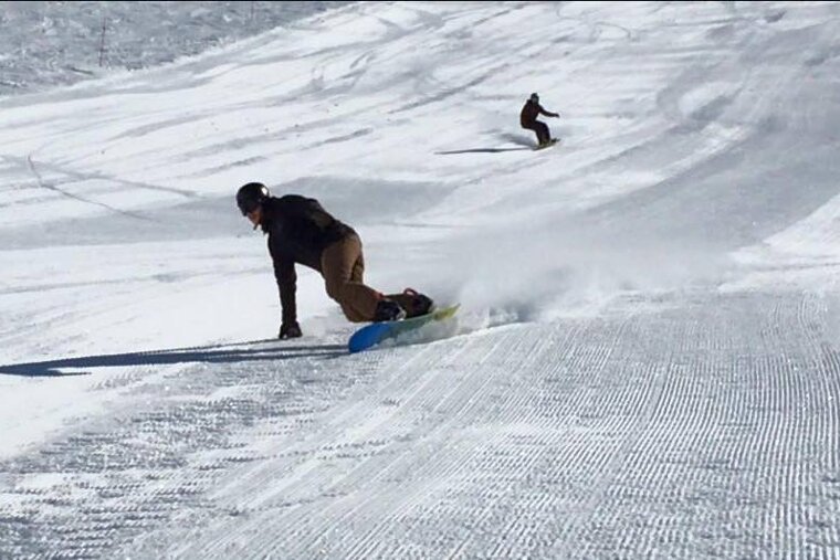 two snowboarders carving down corduroy pistes