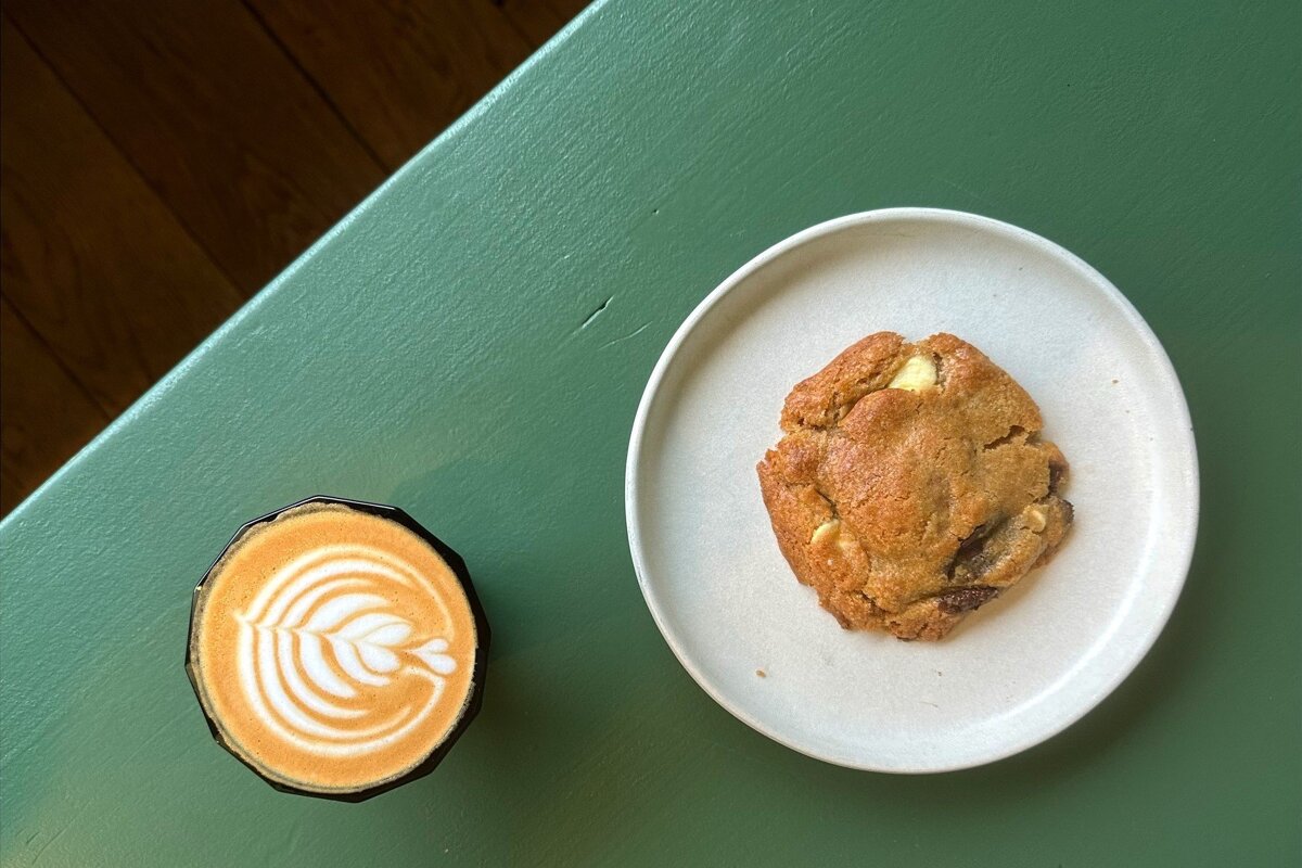 A cup of cappuccino next to a plate of cookie