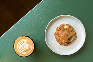 A cup of cappuccino next to a plate of cookie
