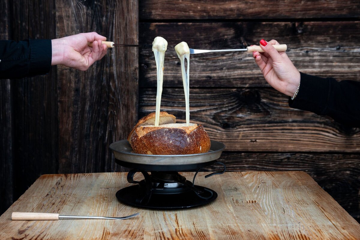 A person is dipping a piece of bread in cheese
