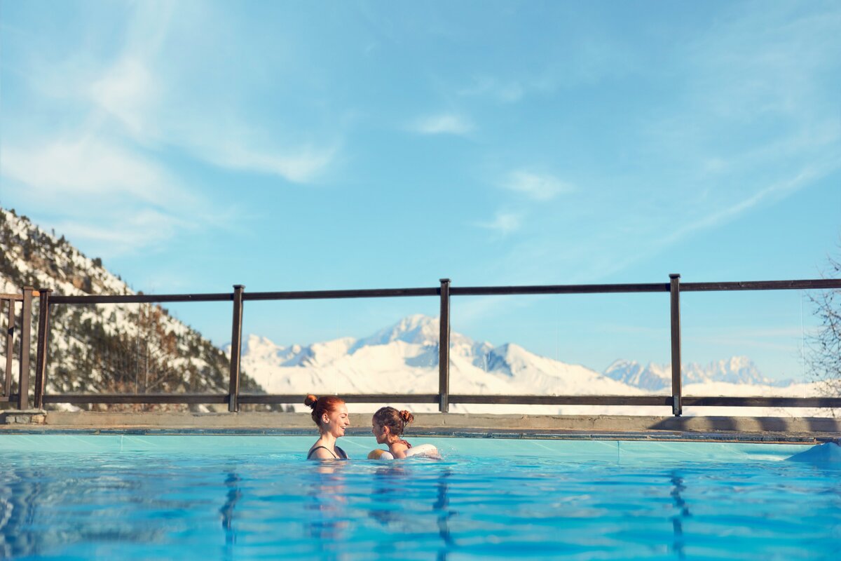 Two women are swimming in a pool with mountains in the background