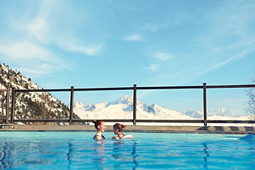 Two women are swimming in a pool with mountains in the background