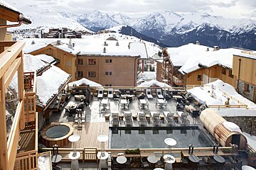 A swimming pool surrounded by chairs and tables with mountains in the background