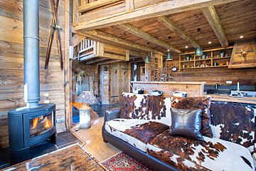 Cozy wooden ski chalet with a lit fireplace, cowhide sofa, rustic kitchen, and decorative skis. Warm, inviting alpine interior.