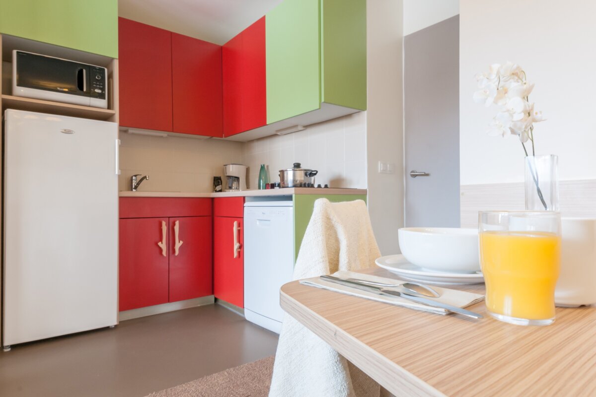 A kitchen with red green and white cabinets and a glass of orange juice