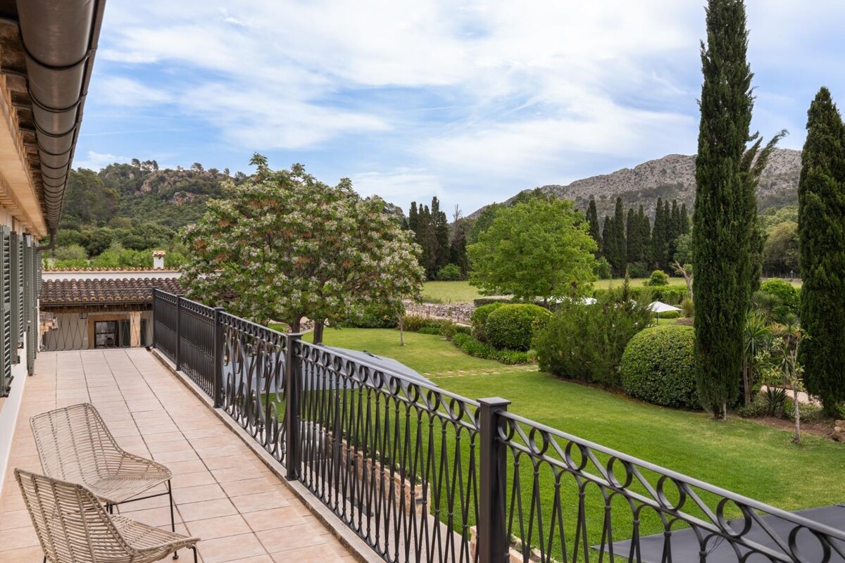 A balcony overlooking a lush green field with trees and mountains in the background