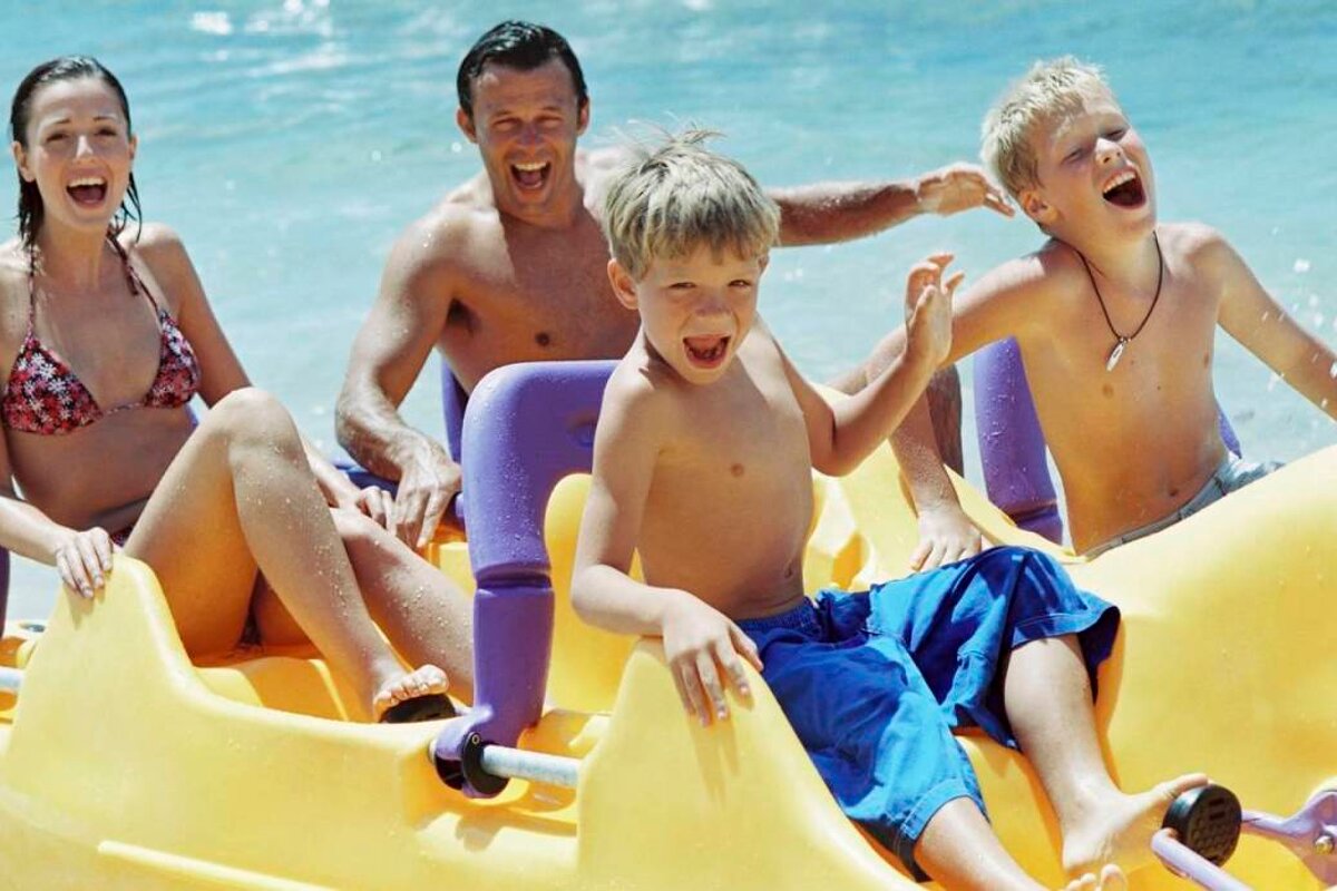 A family is riding a yellow and purple pedal boat on the beach