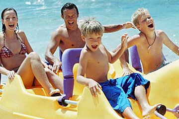 A family is riding a yellow and purple pedal boat on the beach