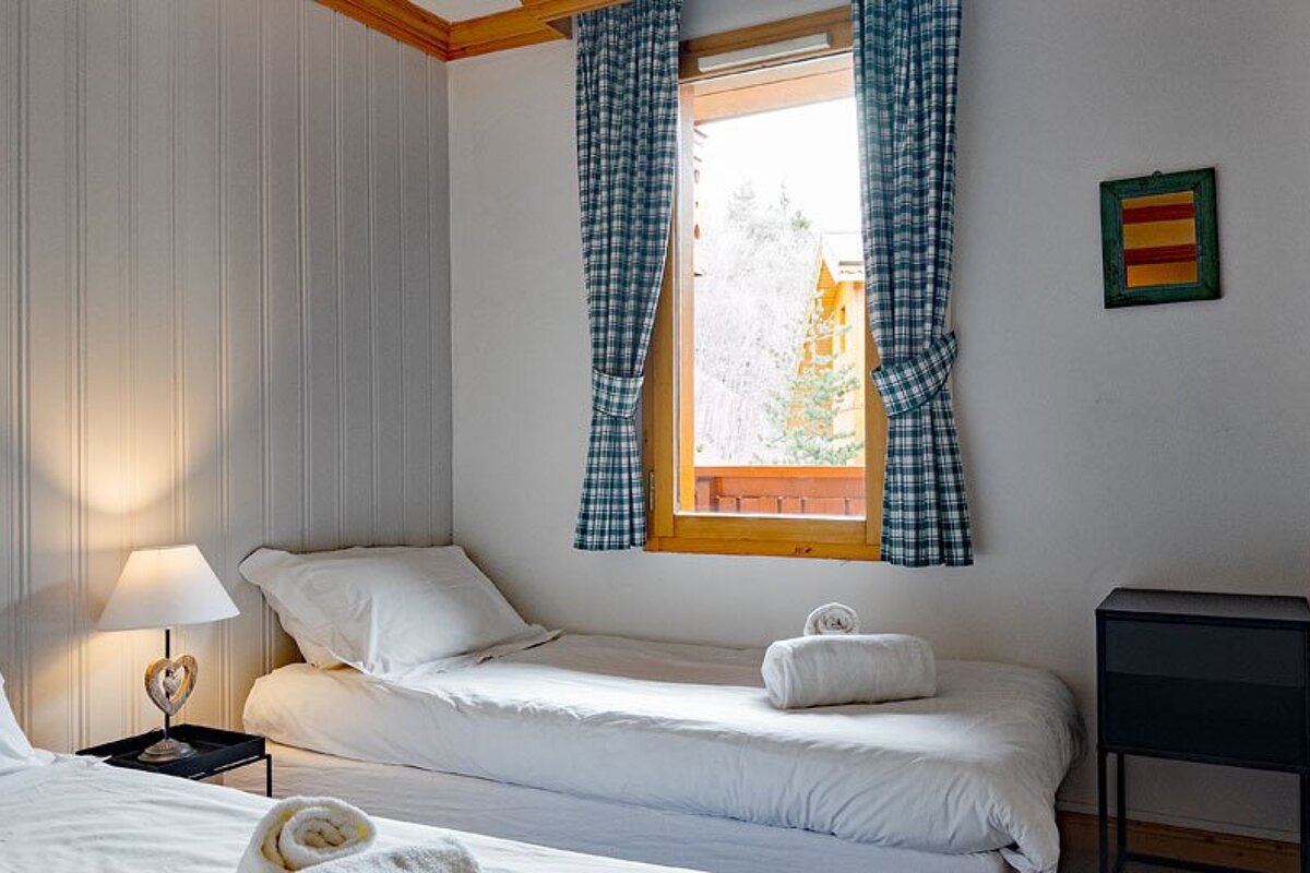A bedroom with two beds and a window with plaid curtains