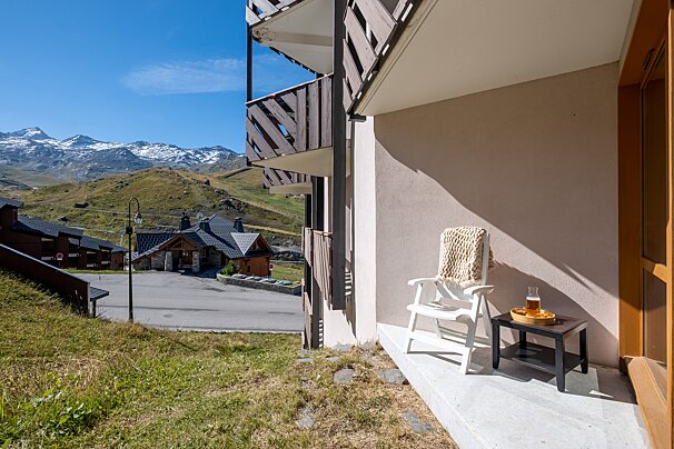 A balcony with a chair and a table with mountains in the background