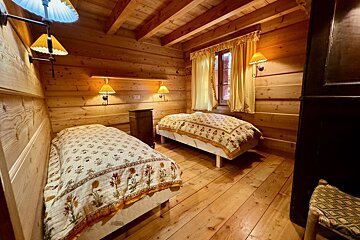 Cozy rustic bedroom with wooden walls/ceiling, two beds with floral quilts, yellow curtains, and warm sconce lighting.