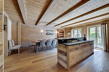 Rustic chalet-style kitchen and dining room with extensive light wood paneling, exposed beams, a large dining table, and a wooden island.