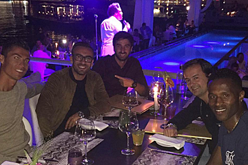 A group of men are sitting at a table in front of a pool
