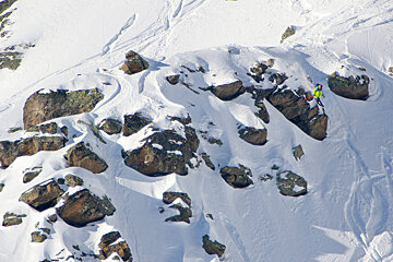 A person in a yellow jacket is skiing down a snowy mountain
