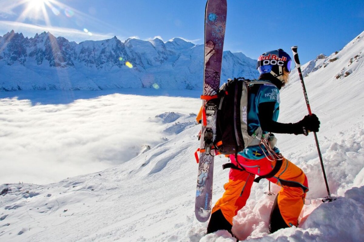 a skier climbing with skis on back and clouded valley below