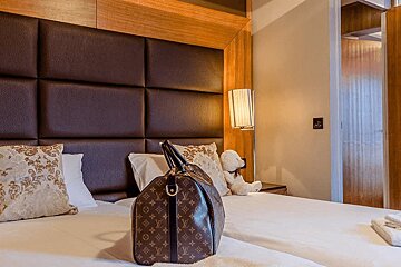 A louis vuitton bag sits on a bed next to a teddy bear
