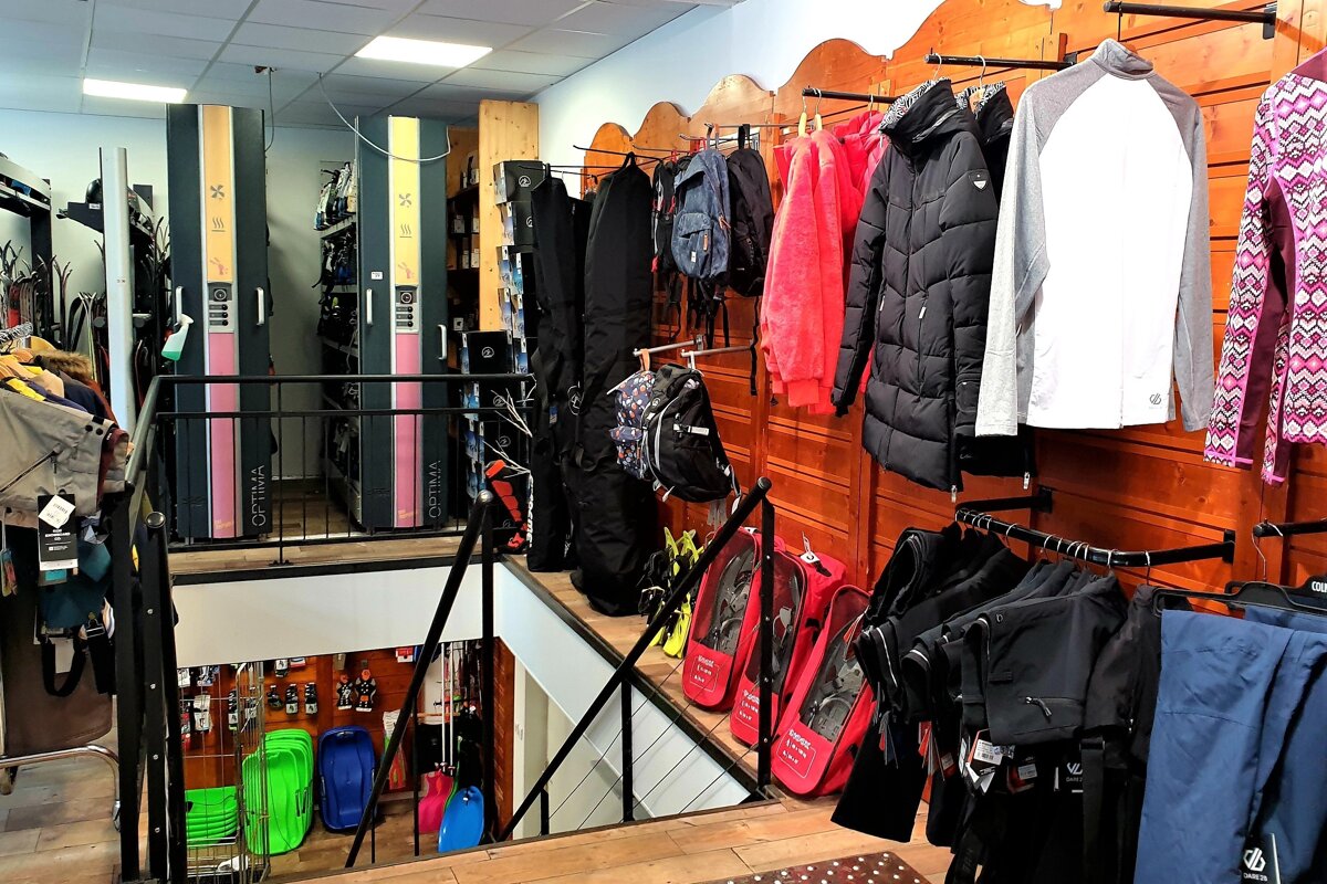 A multi-level ski and winter sports shop with clothing, gear, boot dryers, snowshoes, and sleds displayed on two levels connected by stairs.