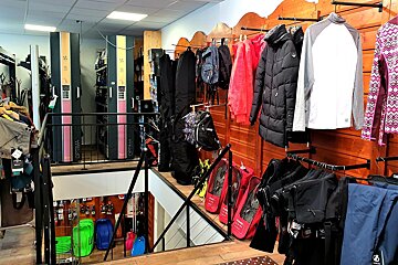 A multi-level ski and winter sports shop with clothing, gear, boot dryers, snowshoes, and sleds displayed on two levels connected by stairs.
