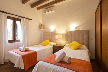 Two beds in a bedroom with orange blankets and yellow pillows